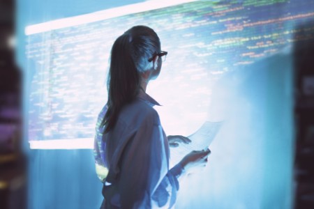 手持文件的商業女性看著投射螢幕上顯示的電腦代碼