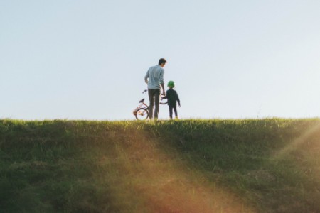 父親在草坡上牽著兒子和腳踏車。